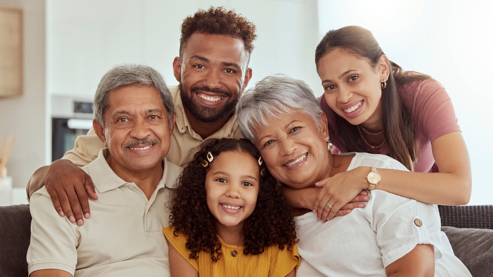 Familia hispana multigeneracional sonriendo en casa: abuelos, padres y una niña