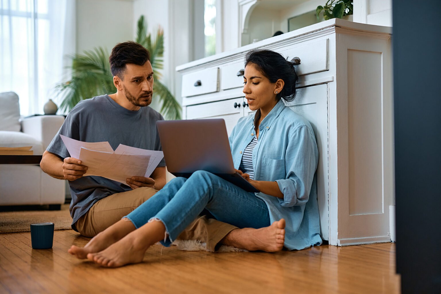 Pareja hispana revisando documentos y una laptop en el piso de su sala